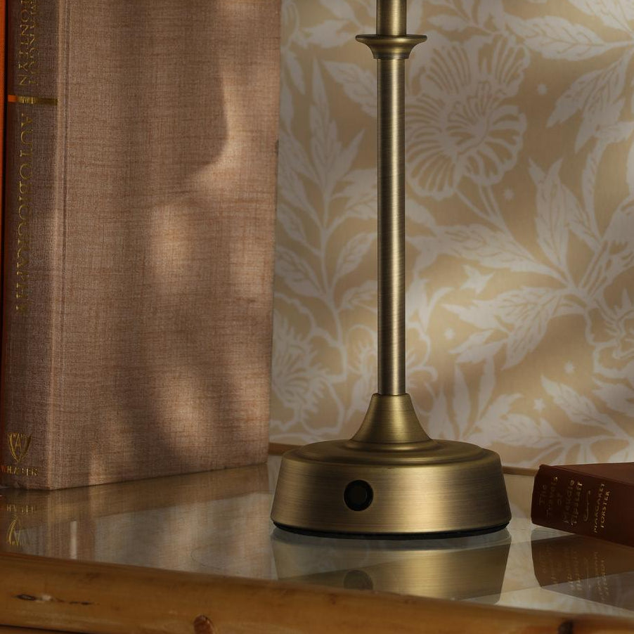 Joules Apsley rechargeable table lamp in matt antique brass on a glass surface next to books