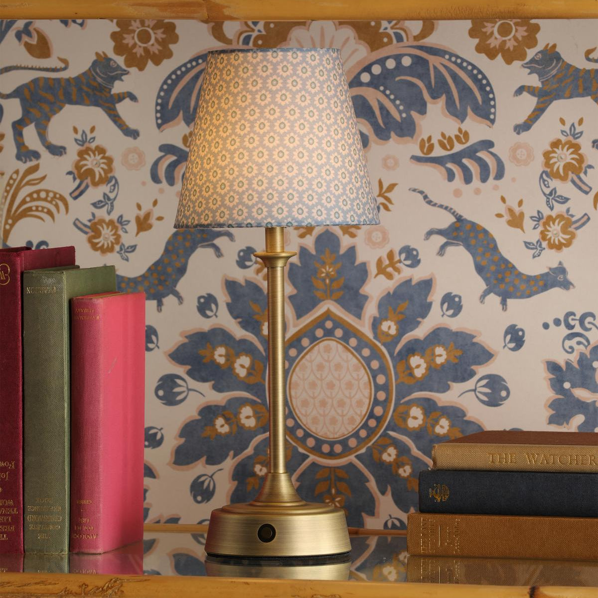 Brass table lamp with a patterned blue fabric shade on a shelf with books