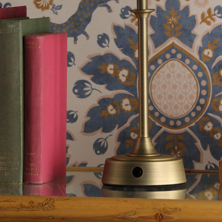 Joules Apsley rechargeable table lamp base in matt antique brass next to books
