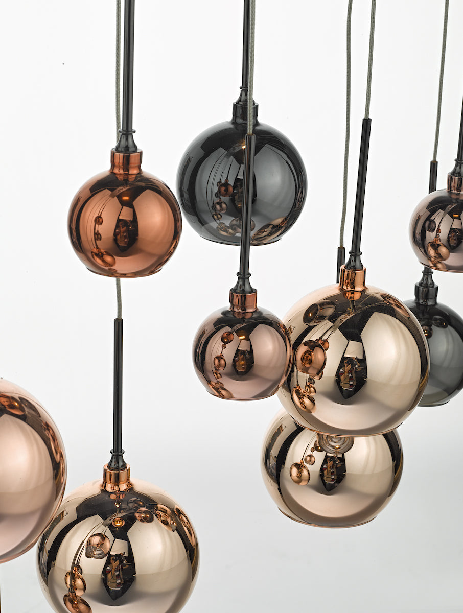Close-up of hanging pendant lights with round, reflective copper and dark gray glass shades.