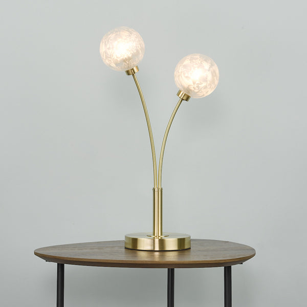 Two-light table lamp with frosted glass shades and a gold finish on a wooden table.