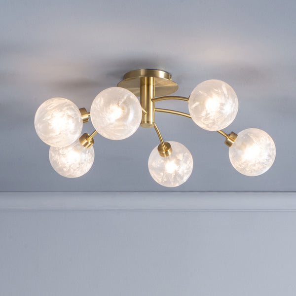 Modern brass ceiling light with six frosted glass globe shades, illuminating a light gray ceiling.