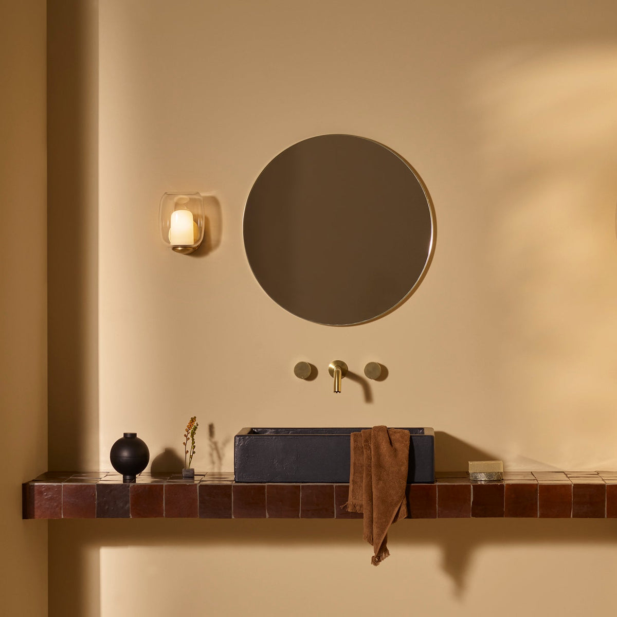 Bathroom with a black rectangular sink, a round mirror, and a gold faucet