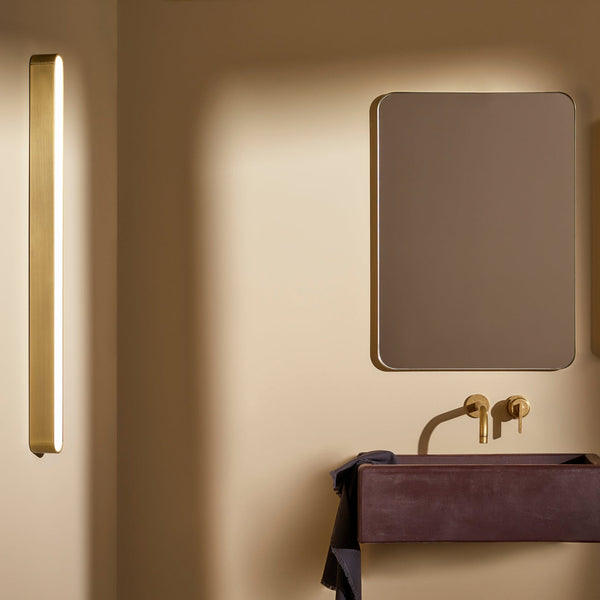 Bathroom with a rectangular mirror, a dark red sink, and brass fixtures. A vertical light fixture is on the left