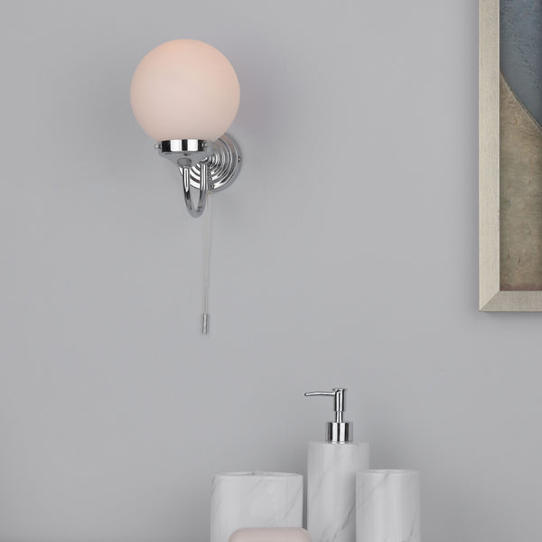 A chrome wall sconce with a spherical opal glass shade and a pull cord switch.