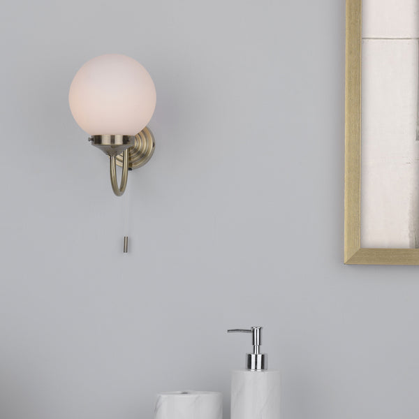 A wall-mounted light fixture with a spherical white shade and a brass base, next to a gold-framed picture.