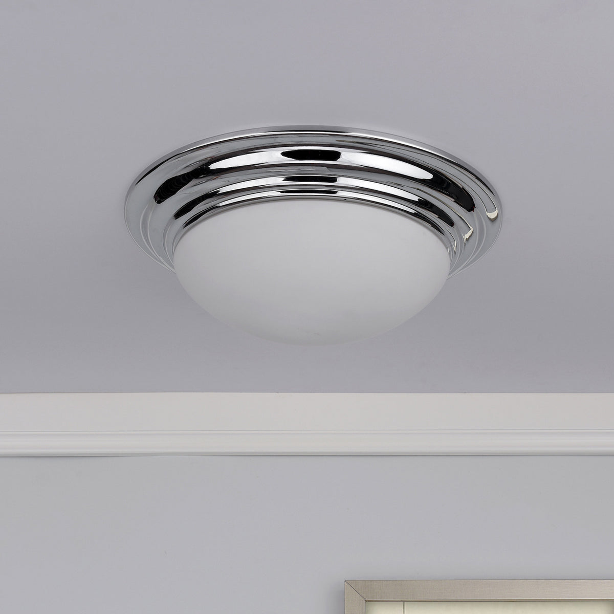 Chrome flush mount ceiling light with a white glass diffuser, installed on a white ceiling.