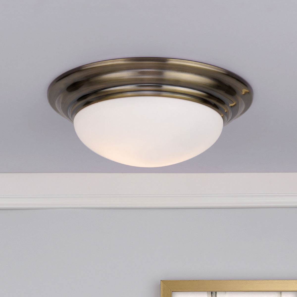 A close-up of a ceiling light fixture with a brass base and a frosted white glass dome.