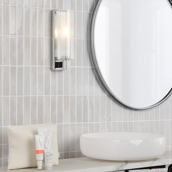 Bathroom vanity with white vessel sink, round mirror, wall sconce, and hair care products on marble countertop