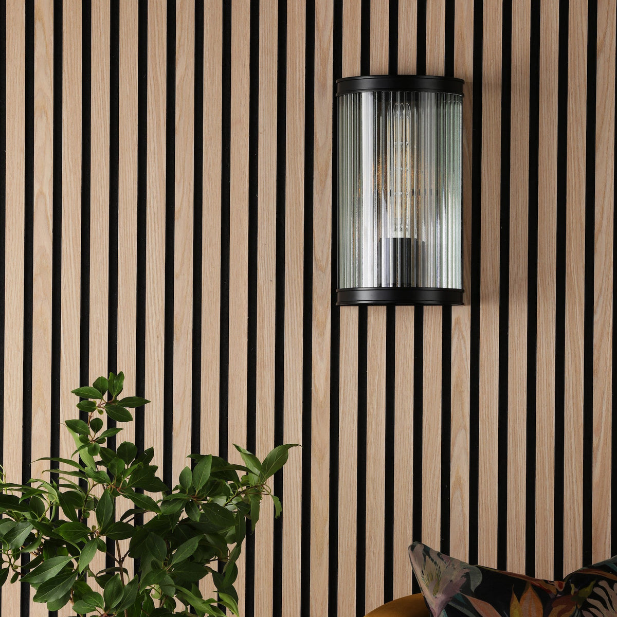 Black and wood panelled wall with a black and glass wall light and a green plant