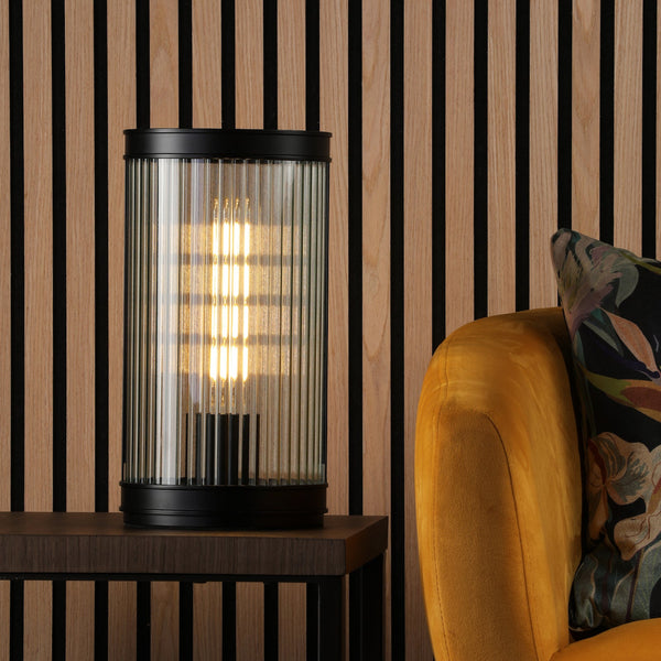 Black and glass table lamp on a dark wood table next to a yellow armchair with a patterned cushion
