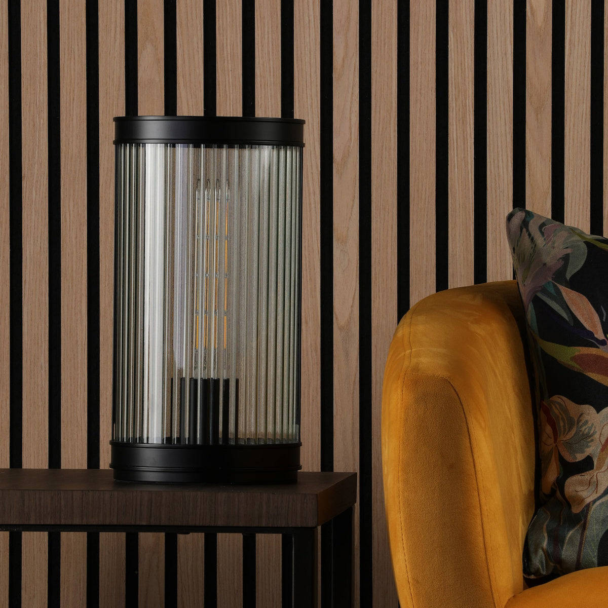 Table lamp with fluted glass shade on a dark wood side table next to a yellow armchair