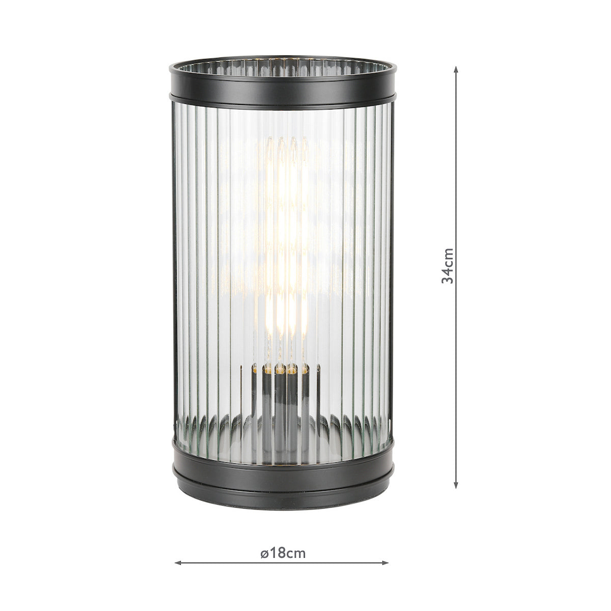 Black metal and fluted glass table lamp with a glowing bulb, 34cm tall and 18cm wide
