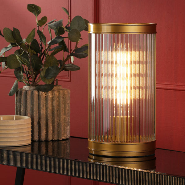 Gold and glass fluted table lamp on a black console table with a plant and candle