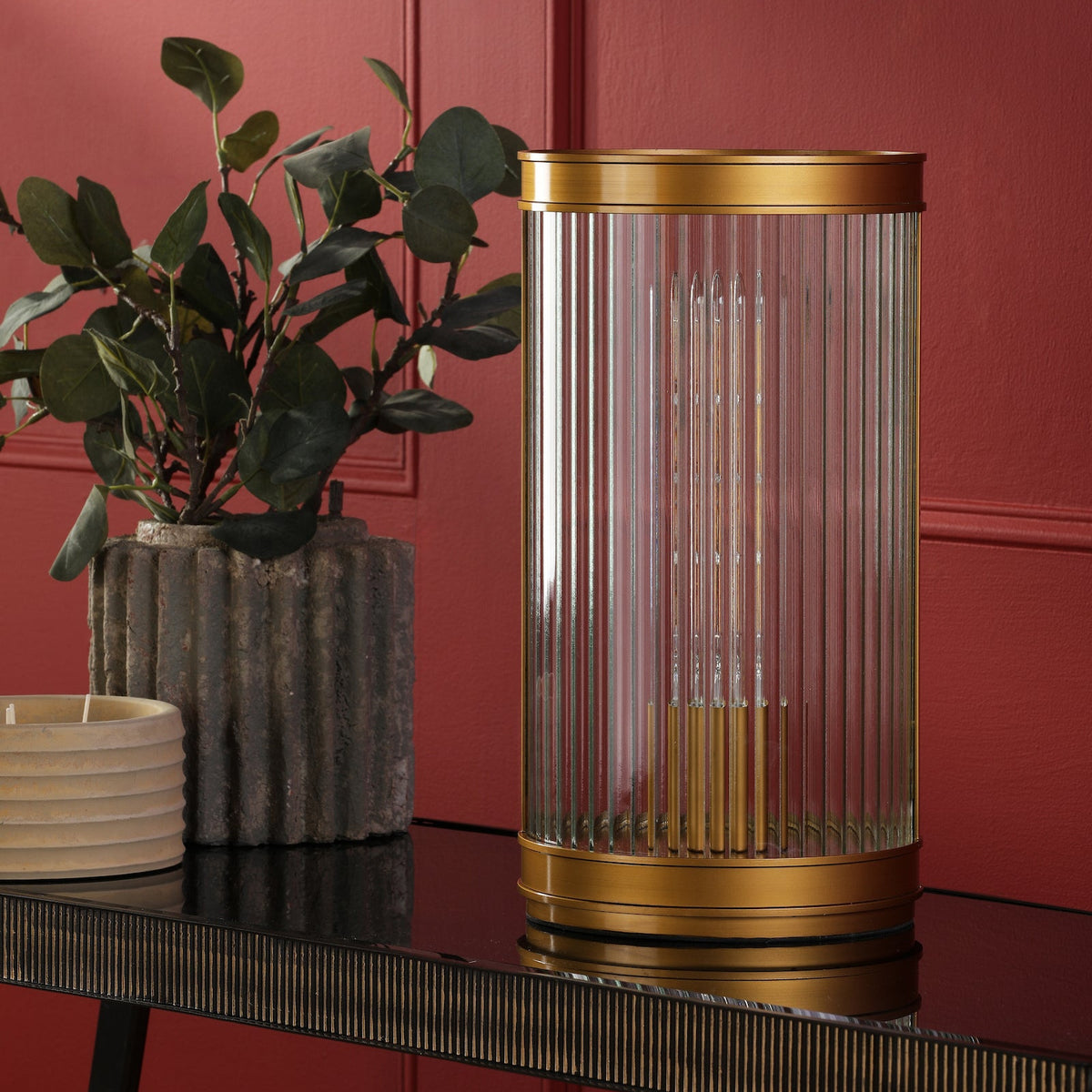 Gold and glass table lamp on a black console table, with a plant and candle in the background
