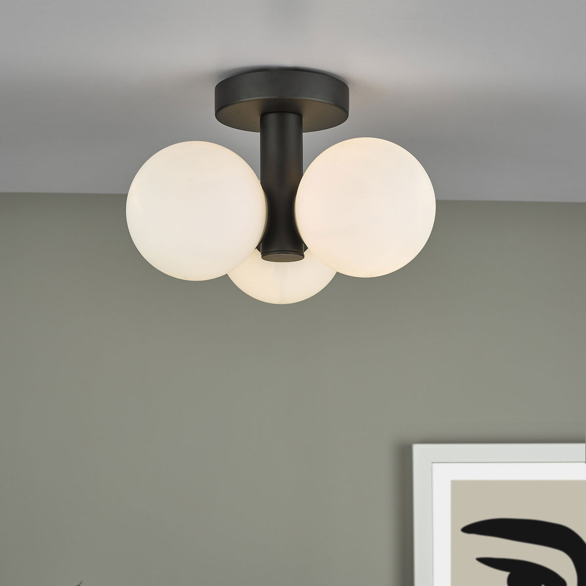 Modern black ceiling light with three white globe shades, illuminating a room with a framed abstract print.