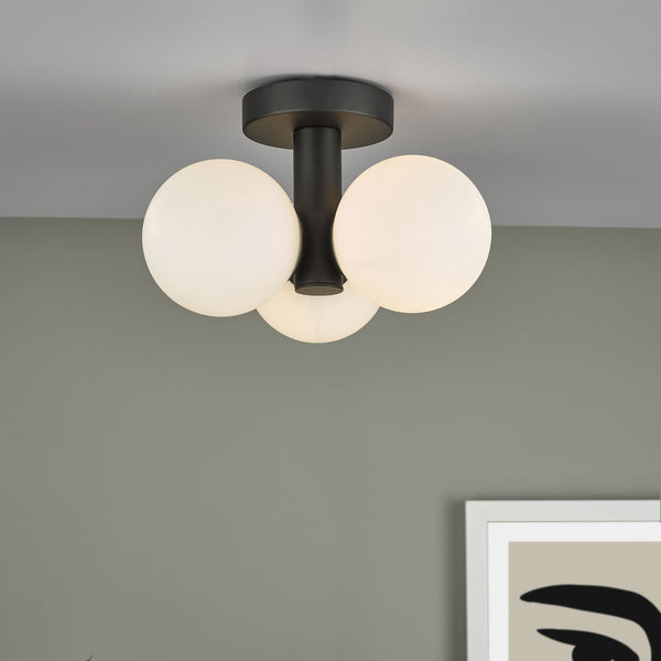 Modern black ceiling light with three white globe shades, illuminating a room with a framed abstract print.