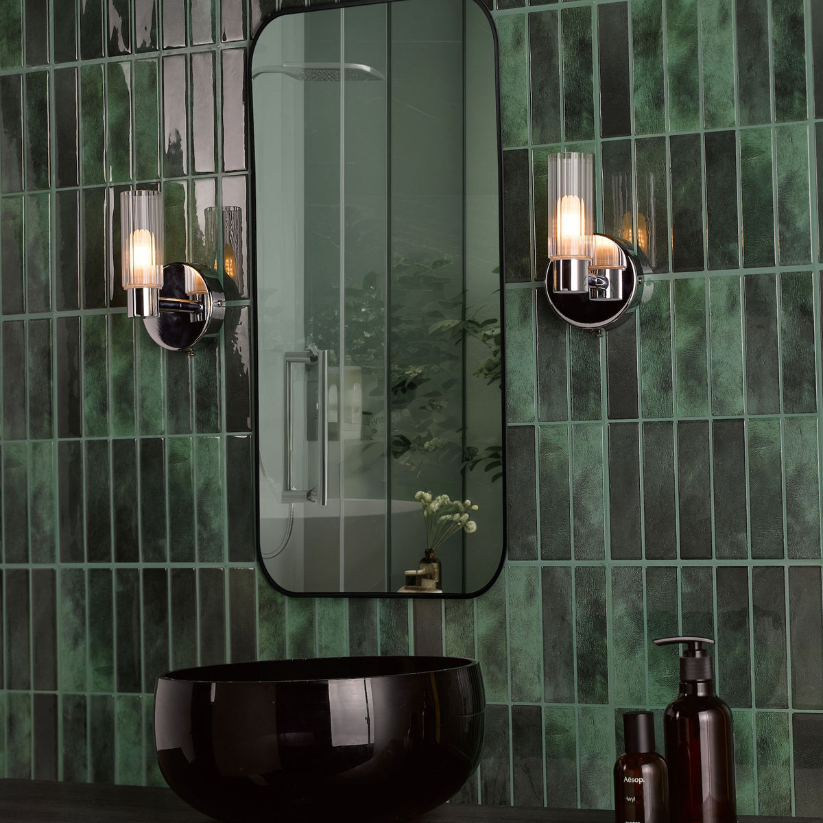 Bathroom with dark green subway tiles, a black mirror, two wall sconces, and a black sink