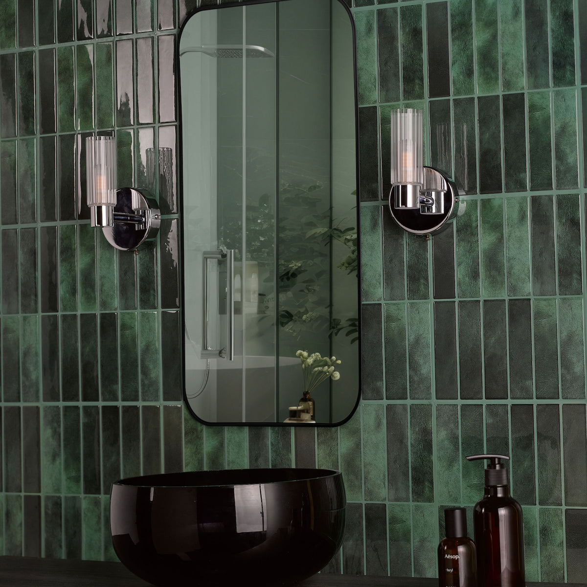 Green tiled bathroom wall with a black mirror, black sink, and two wall sconces