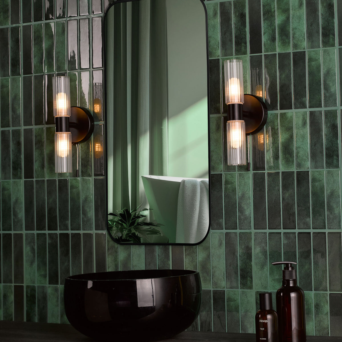 Bathroom with dark green subway tiles, black mirror, black sink, and two wall sconces