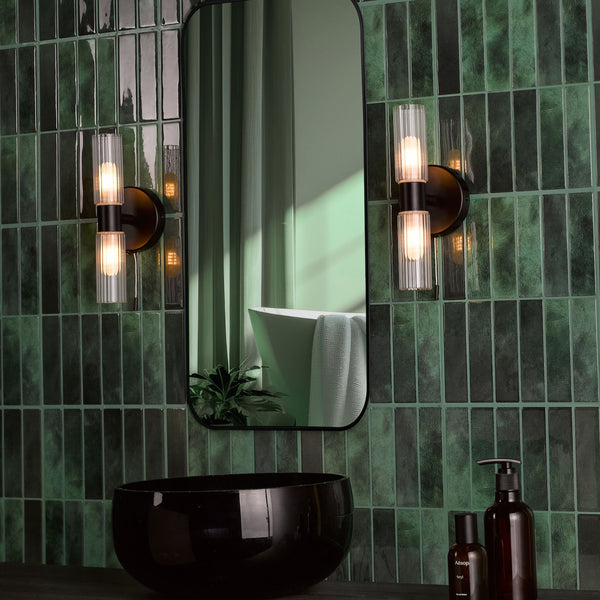 Bathroom with dark green subway tiles, black mirror, black sink, and two wall sconces