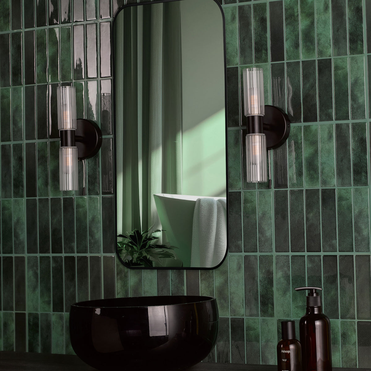 Green tiled bathroom with a black mirror, black sink, and two wall sconces
