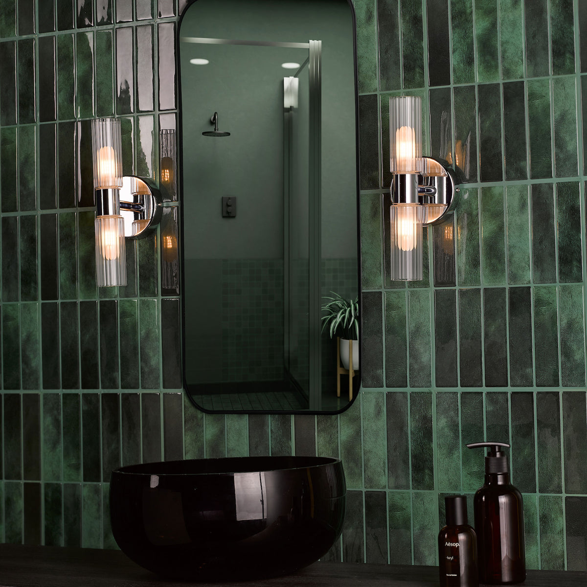 Bathroom with dark green subway tiles, black sink, mirror, and two wall-mounted lights