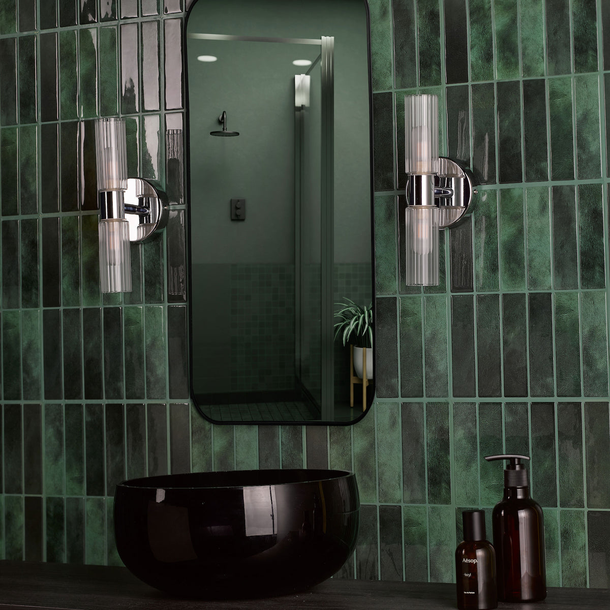 Bathroom with dark green subway tiles, black vessel sink, and two wall sconces flanking a mirror