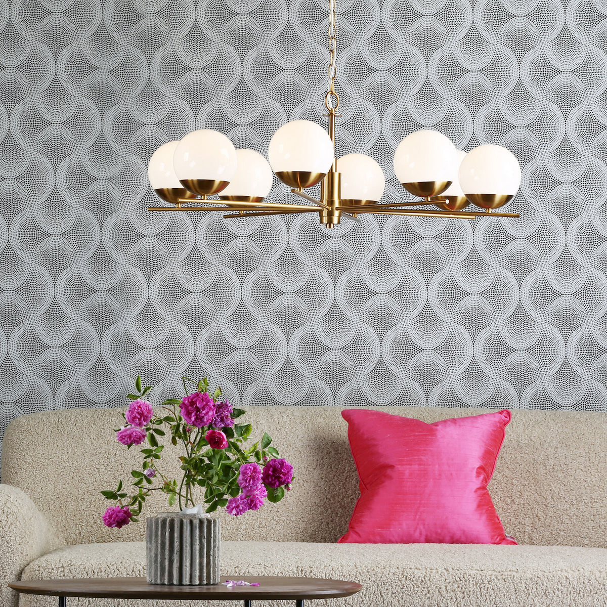 Living room with a gold chandelier, a beige sofa, a pink cushion, and a vase of pink flowers