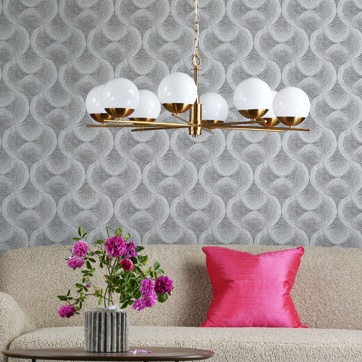 Black and white dotted wallpaper with a gold chandelier, a beige sofa, a pink pillow, and pink flowers