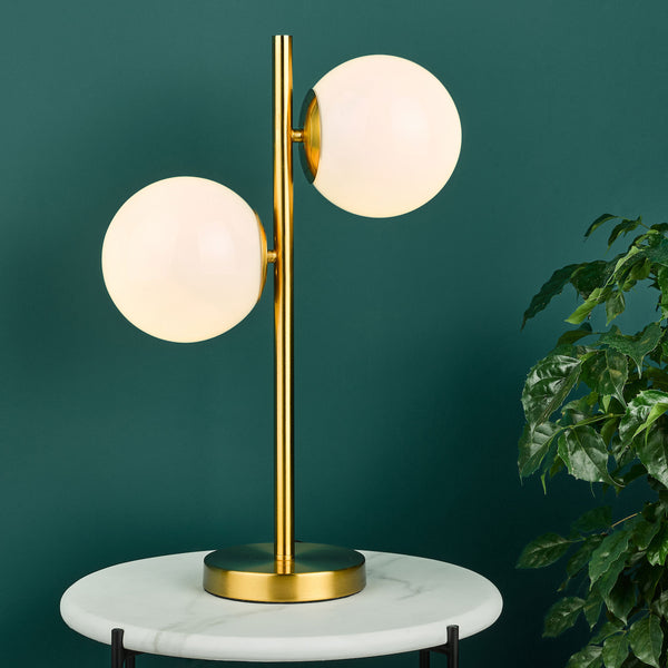 Gold table lamp with two spherical white glass shades on a white marble table