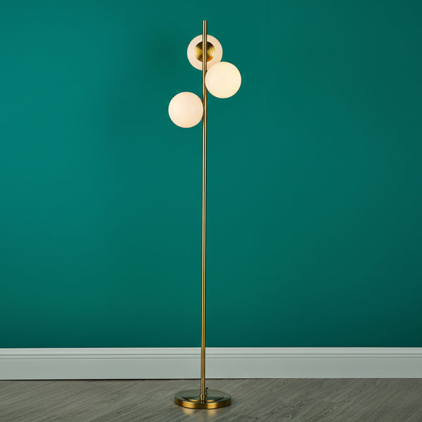 Gold floor lamp with three spherical white glass shades against a teal wall