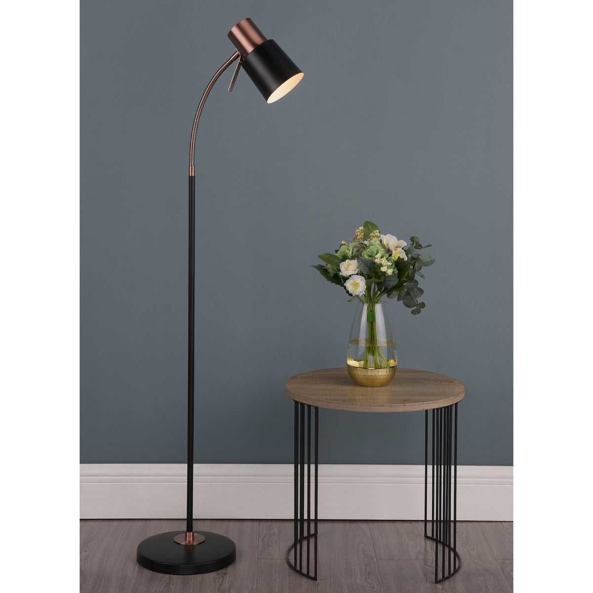 Black and copper floor lamp next to a round wooden side table with a vase of flowers.