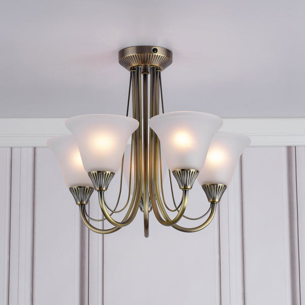 Antique brass chandelier with five frosted glass shades, casting a warm glow on a white ceiling.