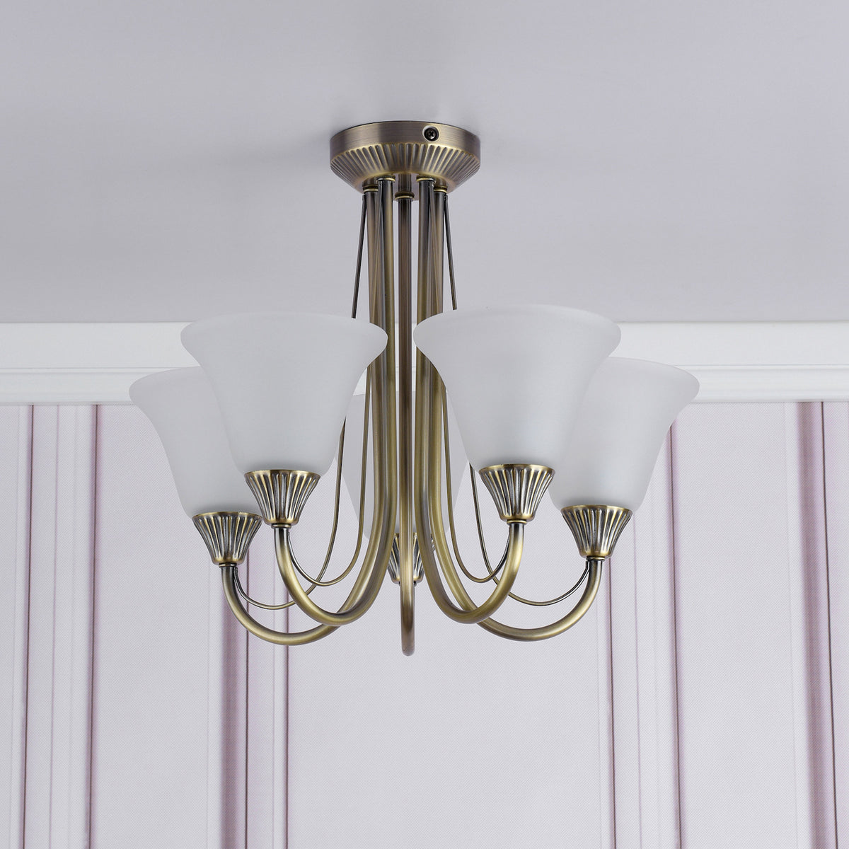 Antique brass chandelier with five frosted glass shades, mounted on a white ceiling with striped wallpaper.