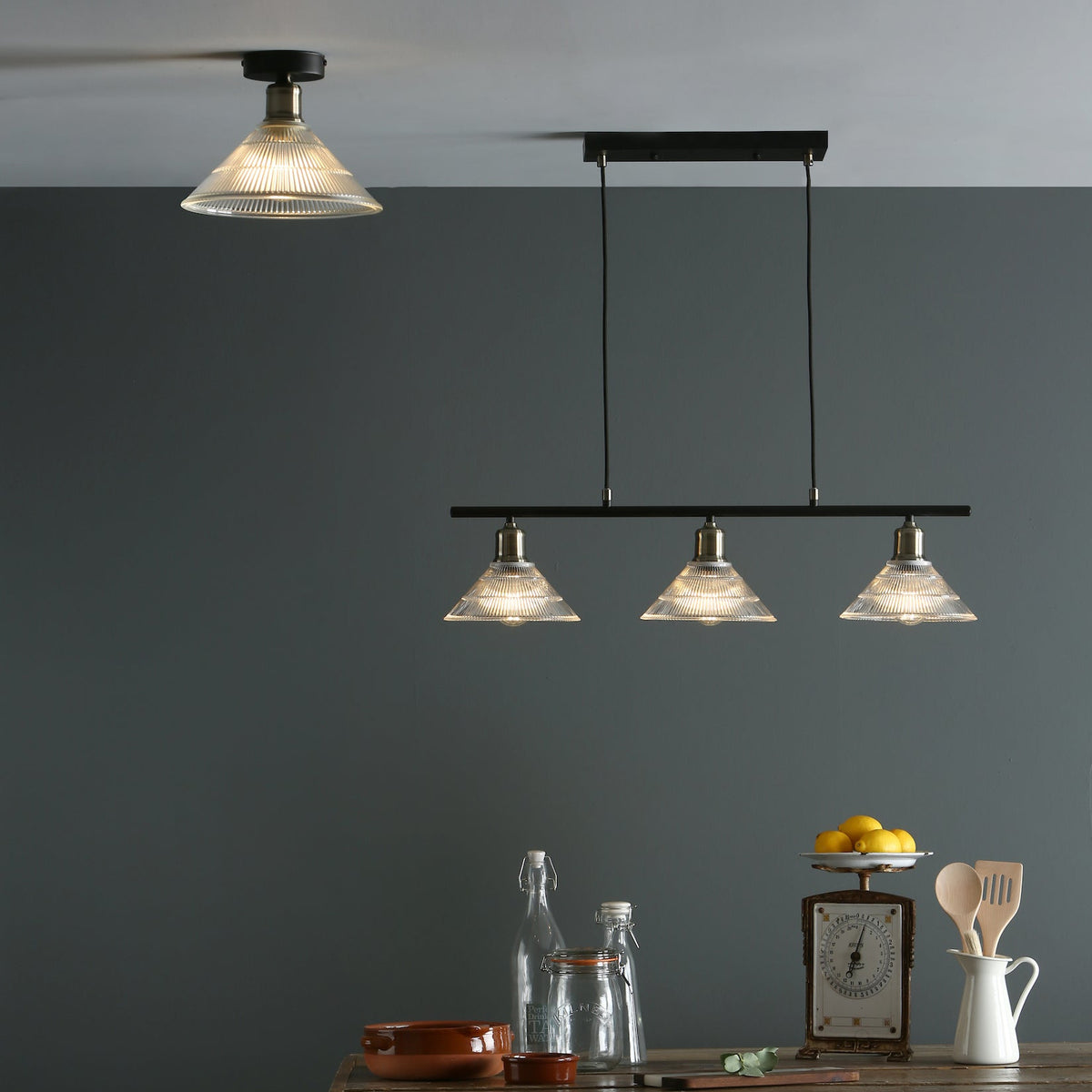 Two ceiling lights with clear glass shades, one single and one with three lights, above a wooden table