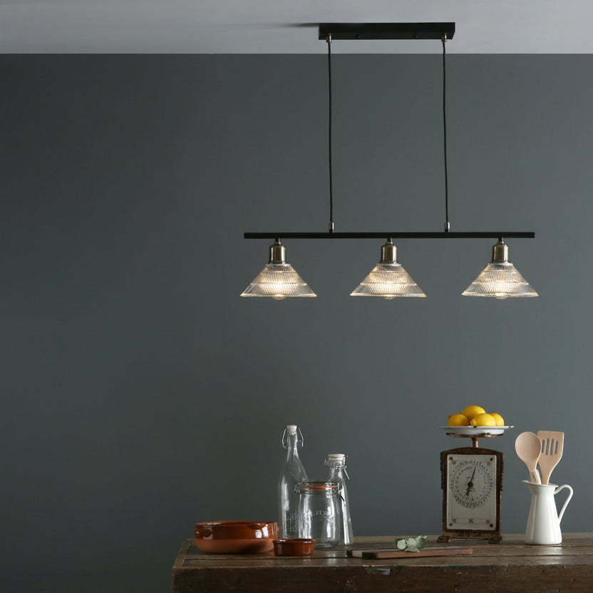 Three clear glass pendant lights hanging above a wooden table with kitchen items