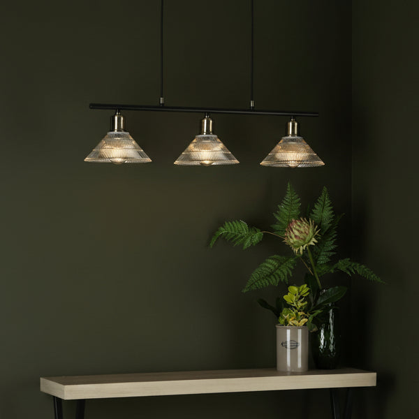 Three glass pendant lights with brass fittings on a black bar, above a wooden console table with plants
