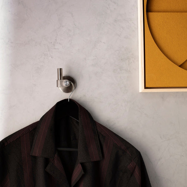 Black shirt with red stripes hanging on a silver wall hook, with a yellow framed artwork on the right