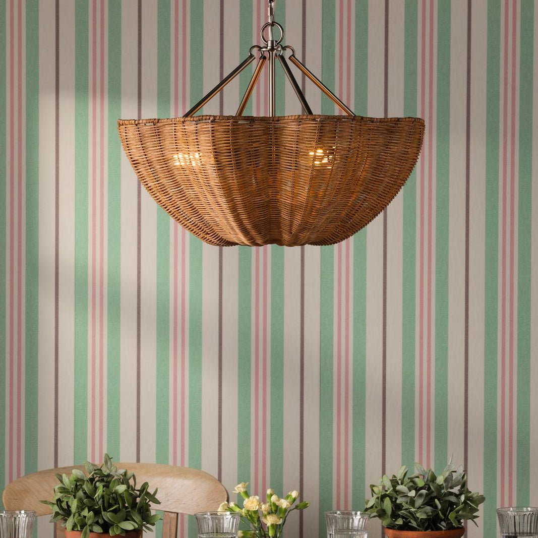 Woven rattan bowl pendant light with metal hardware hanging against striped wallpaper