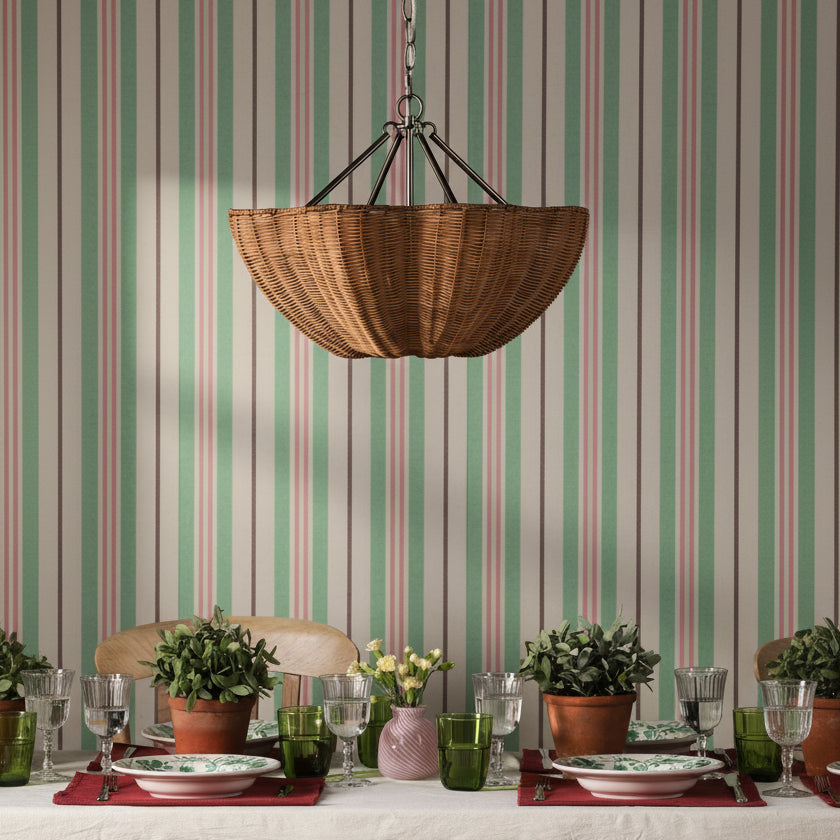 Woven rattan pendant light hanging above a dining table set with potted plants and glassware against striped wallpaper
