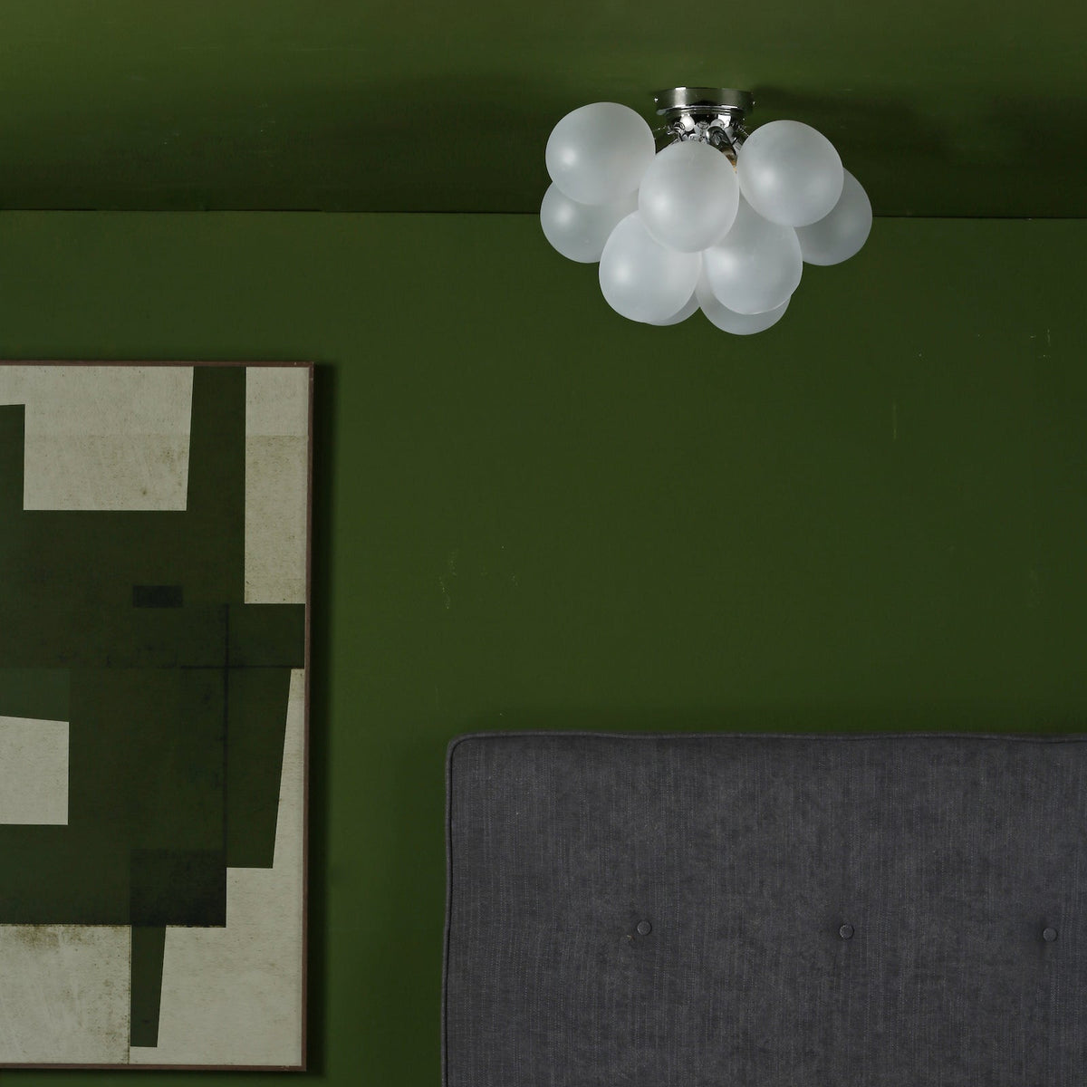 A ceiling light with multiple white spherical shades, a dark green wall, and a grey upholstered headboard