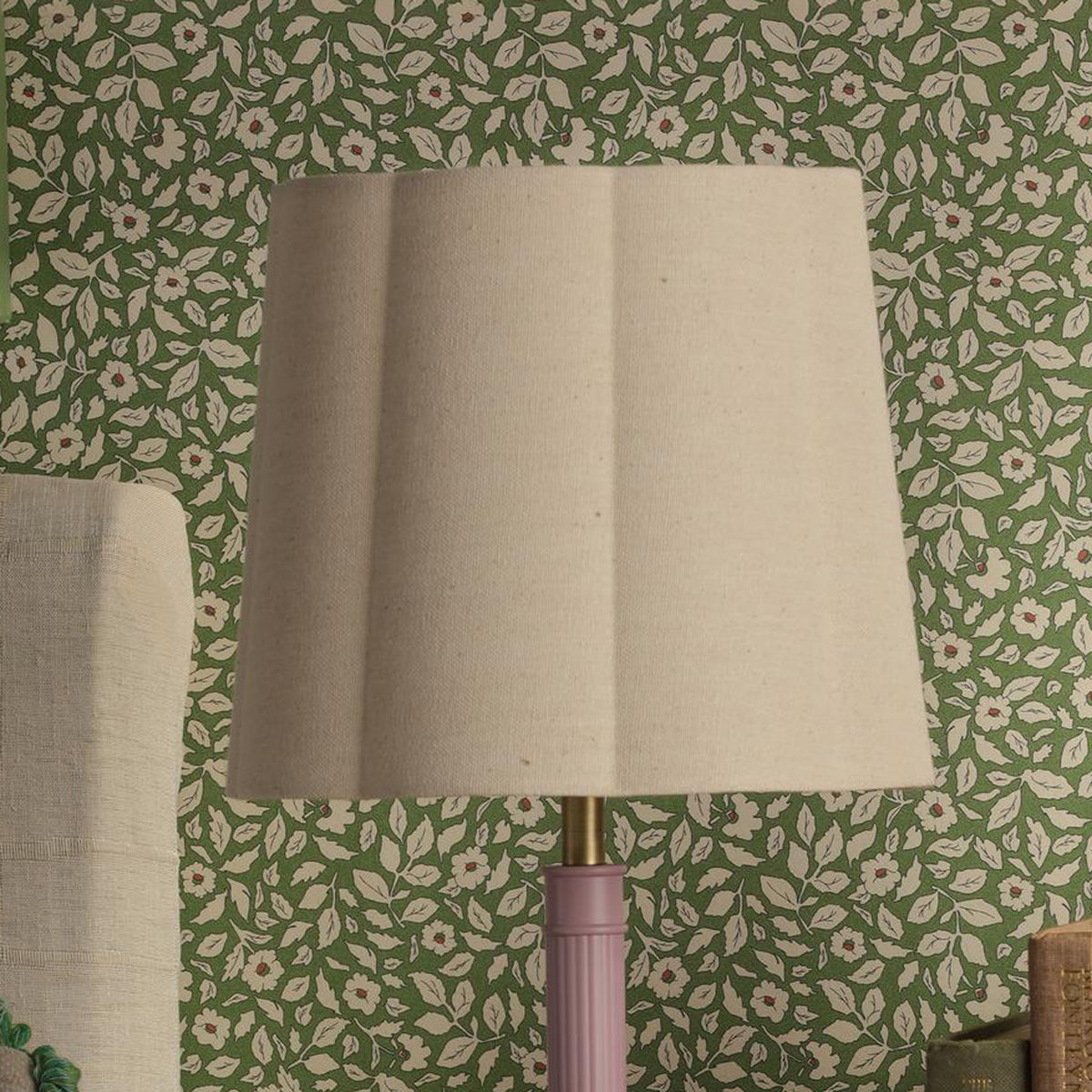 Beige fabric lampshade on a pink fluted lamp base against green floral wallpaper