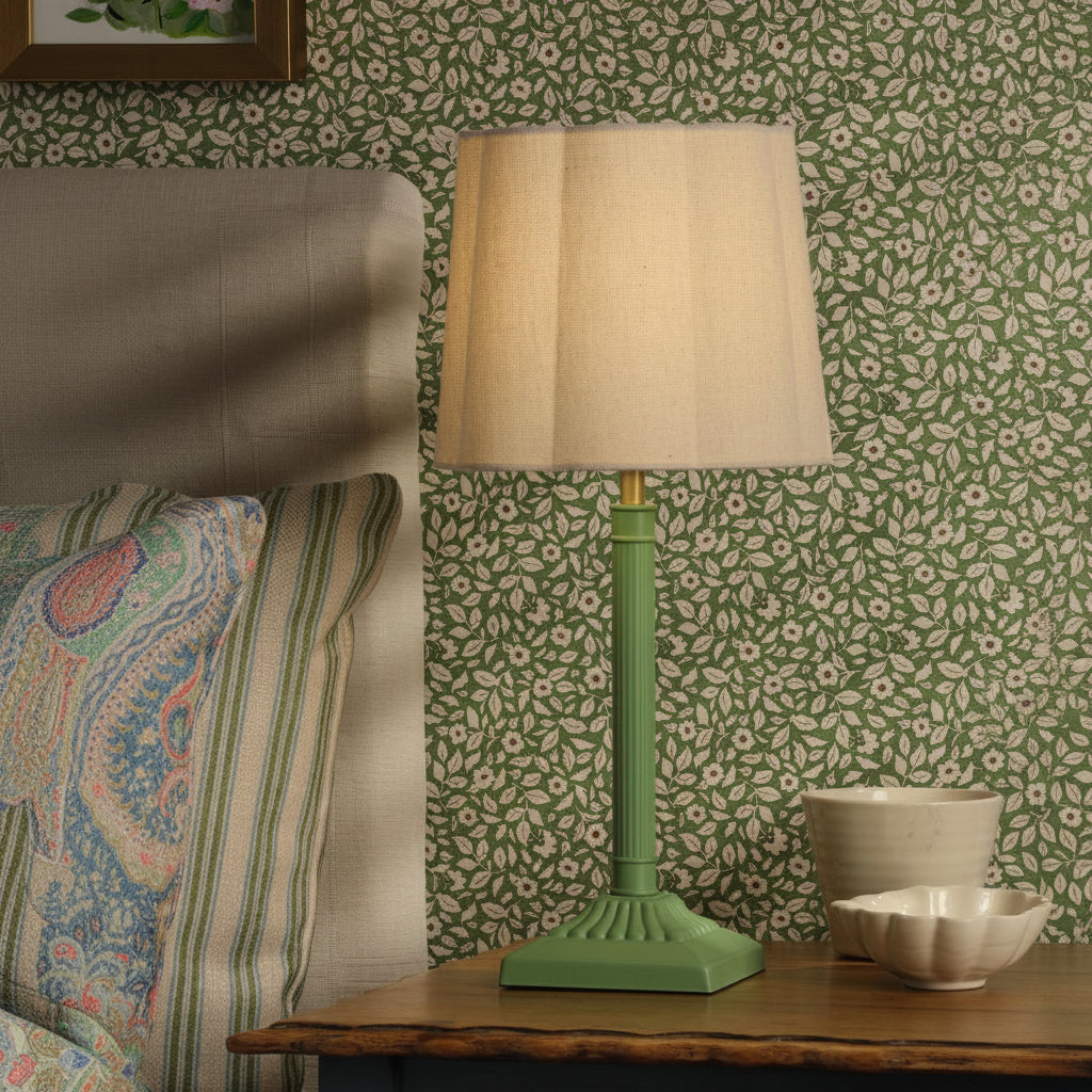 Green table lamp with a pleated fabric shade on a wooden nightstand