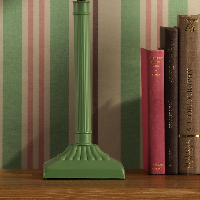 Joules Buscot table lamp in matt green with a fluted base standing on a wooden shelf next to books