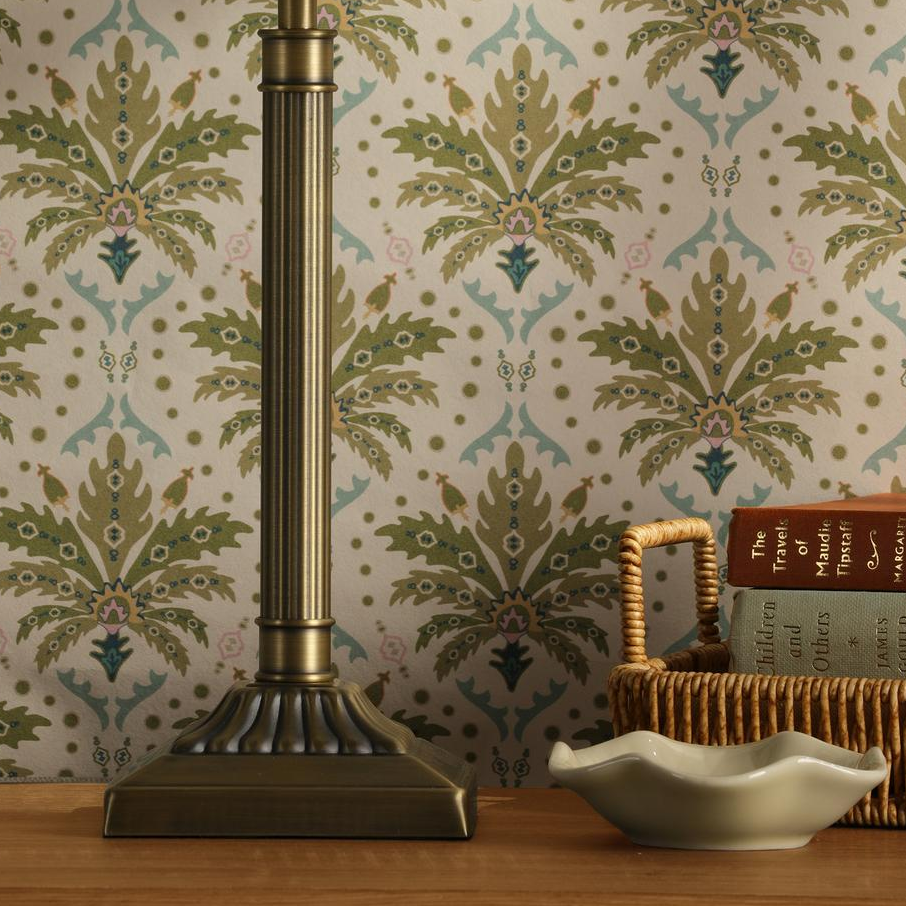 Brass lamp base with books and a small dish against patterned wallpaper