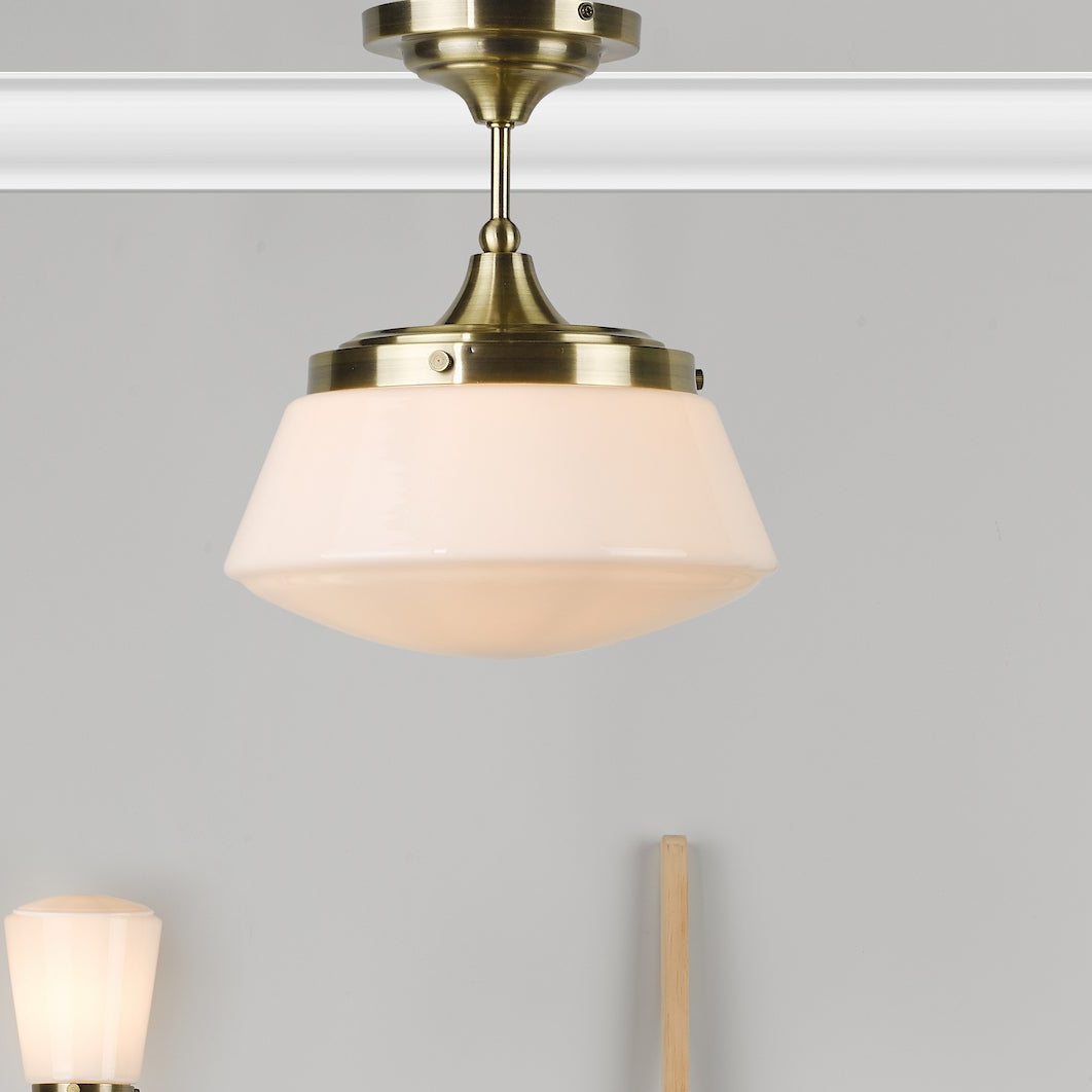A close up of a brass ceiling light with a white glass shade