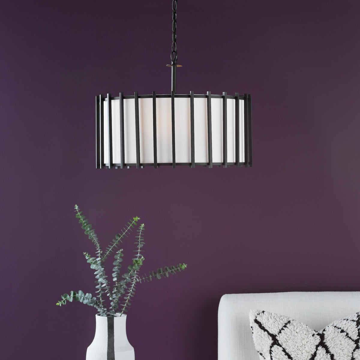 Black metal chandelier with white fabric shade, eucalyptus in a white vase, and a white sofa with a black and white pillow