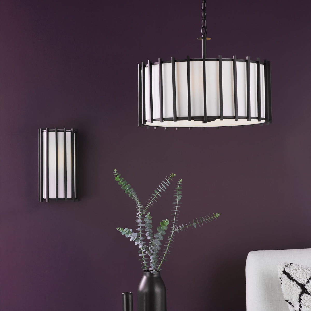 Black and white pendant light and wall sconce on a deep purple wall, with a vase of eucalyptus