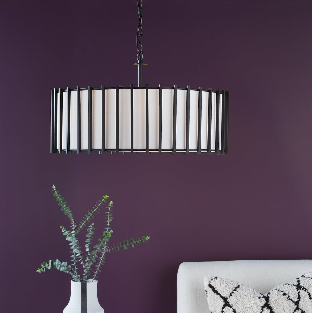 Black metal chandelier with white fabric shade above a white vase with eucalyptus